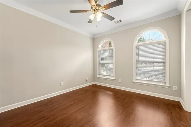 an empty room with wooden floor chandelier fan and windows