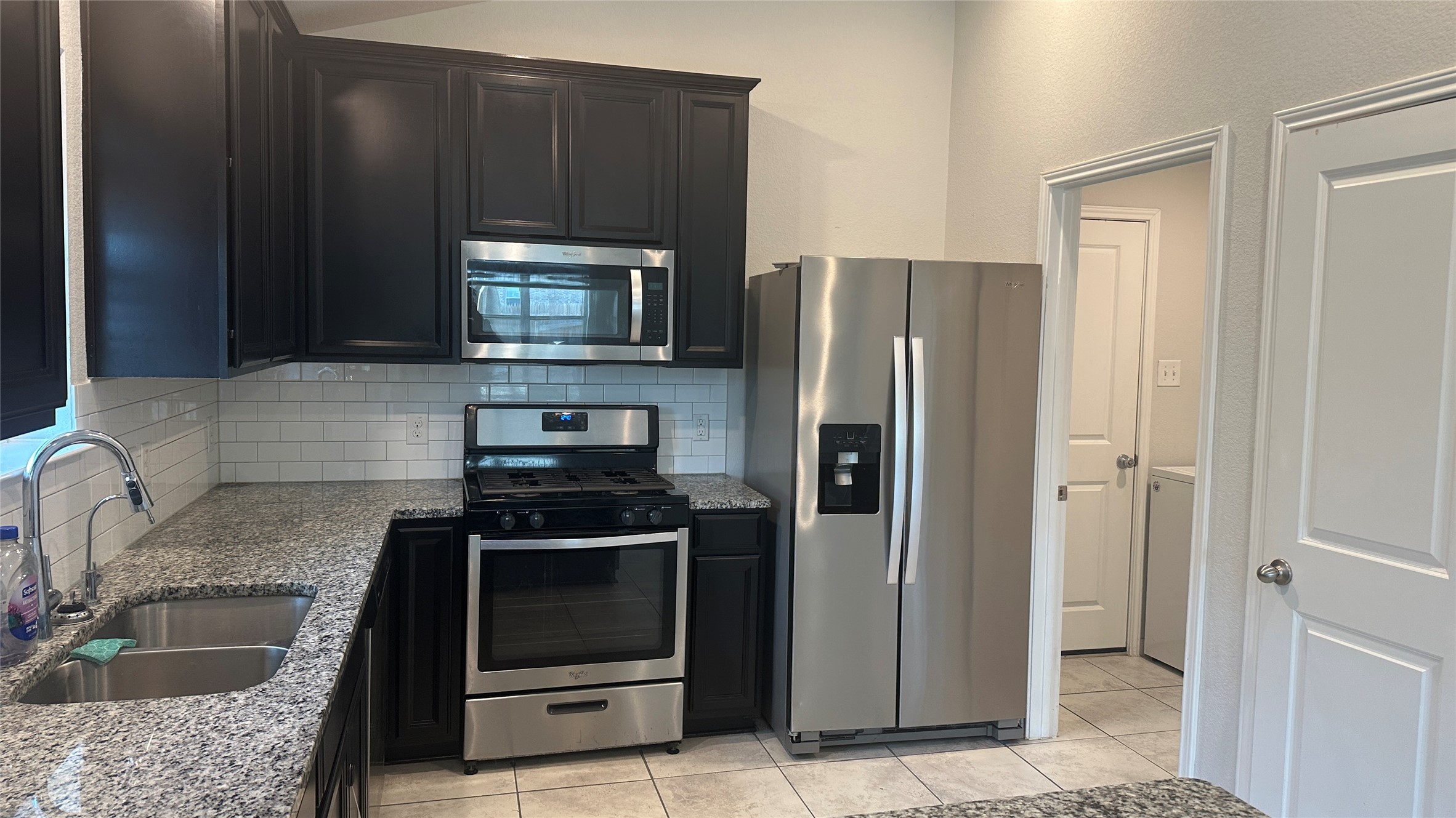 12321 Caldera Way Manor, TX 78653 - Photo 13 of 18 Kitchen with stainless steel appliances, light stone counters, decorative backsplash, light tile patterned floors, and dark cabinetry