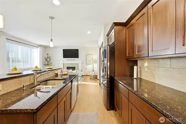 a kitchen with stainless steel appliances granite countertop a stove top oven a refrigerator a dining table and chairs with wooden floor