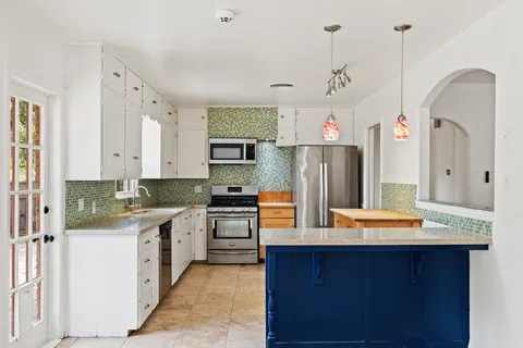 a kitchen with stainless steel appliances granite countertop a refrigerator a sink dishwasher a stove and white cabinets with wooden floor