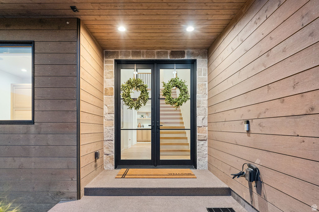 1400 Weber Wild Road Oakley, UT 84055 - Photo 6 of 55 Modern architectural entrance featuring dark-framed double glass doors, stone facade accents, horizontal wood-finish siding, and a wood-panelled ceiling with recessed lighting