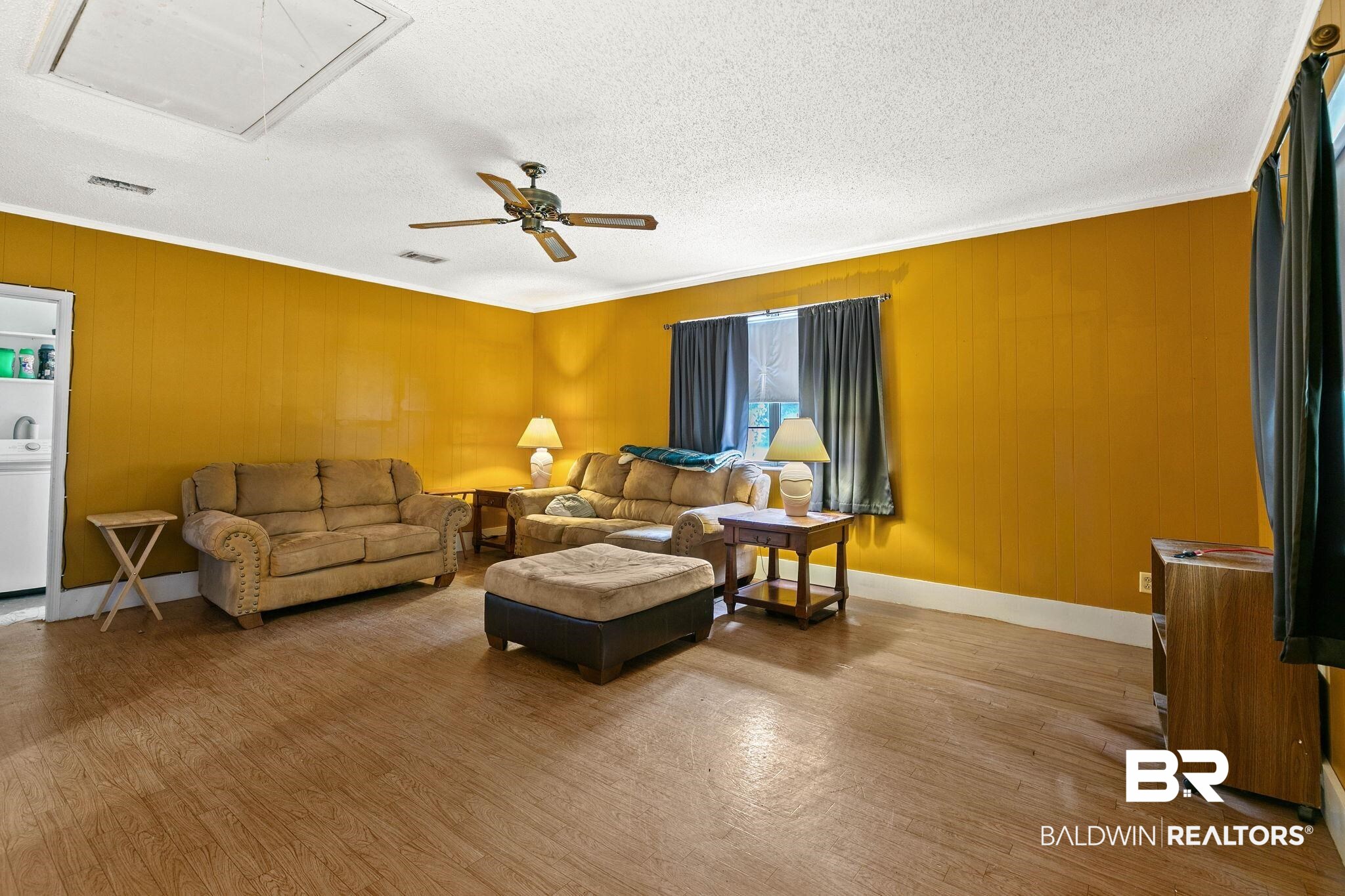 13653 Roberts Road Loxley, AL 36551 - Photo 15 of 33 Spacious living area featuring wood-finish flooring, a ceiling fan with light fixture, and a window with dark drapery