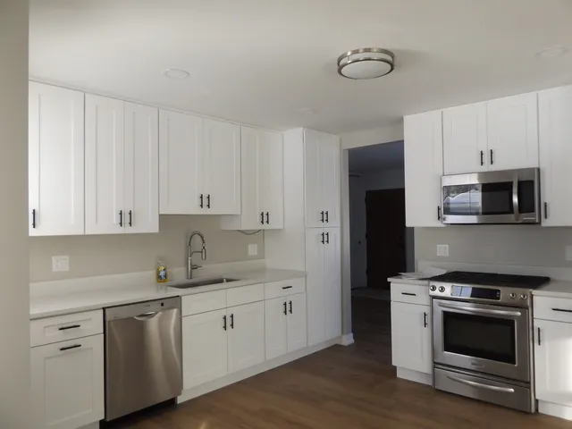 a kitchen with stainless steel appliances granite countertop a sink a stove a refrigerator and white cabinets