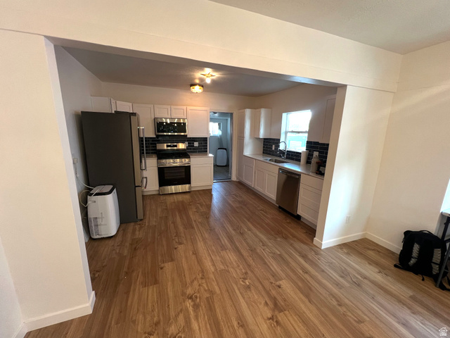 545 23rd Street Ogden, UT 84401 - Photo 2 of 28 Kitchen featuring wood-finish flooring, white cabinetry, dark subway tile backsplash, and stainless steel appliances