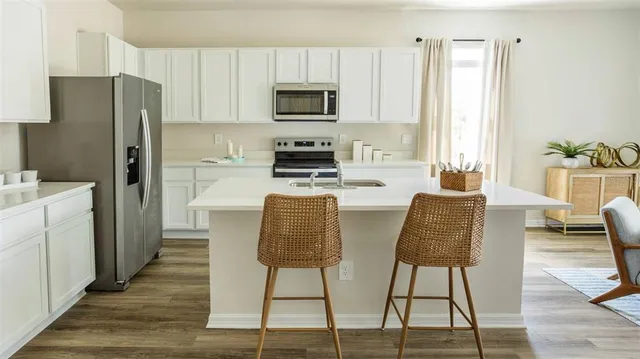 a kitchen with stainless steel appliances granite countertop a refrigerator a stove top oven a sink dishwasher and white cabinets with wooden floor