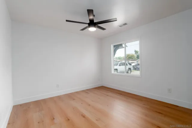 an empty room with wooden floor ceiling fan and windows