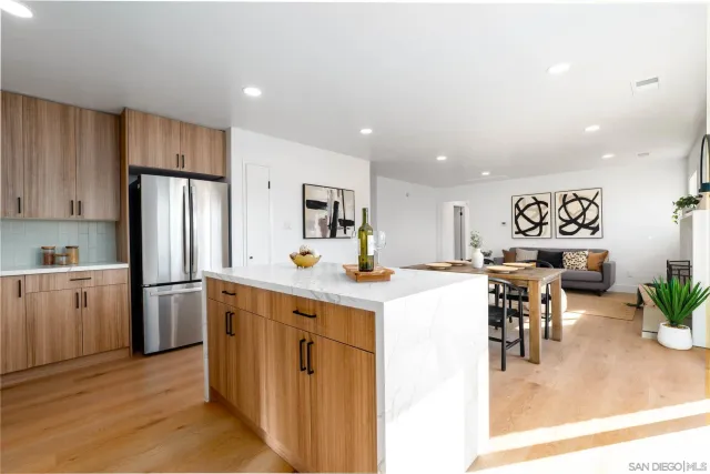 a kitchen with stainless steel appliances kitchen island granite countertop a refrigerator a stove a sink a dining table and chairs with wooden floor