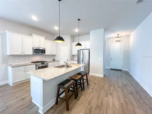 a kitchen with stainless steel appliances granite countertop a refrigerator a sink dishwasher a stove and white countertops with wooden floor