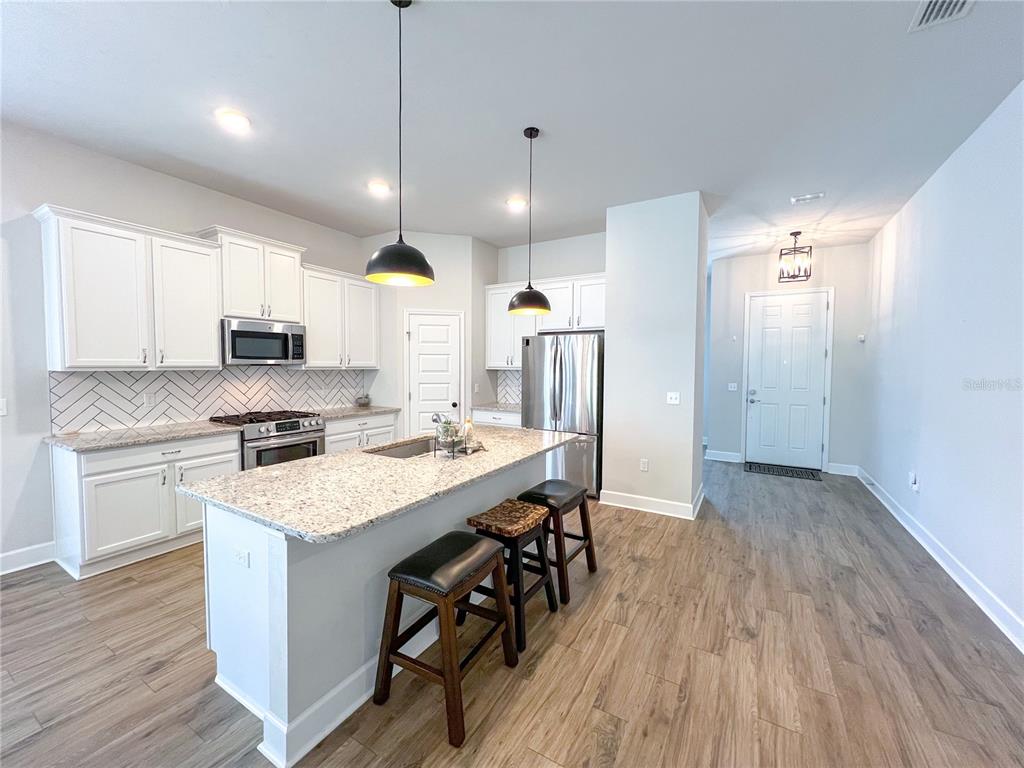 9340 Southwest 67th Lane Gainesville, FL 32608 - Photo 3 of 16 a kitchen with stainless steel appliances granite countertop a refrigerator a sink dishwasher a stove and white countertops with wooden floor