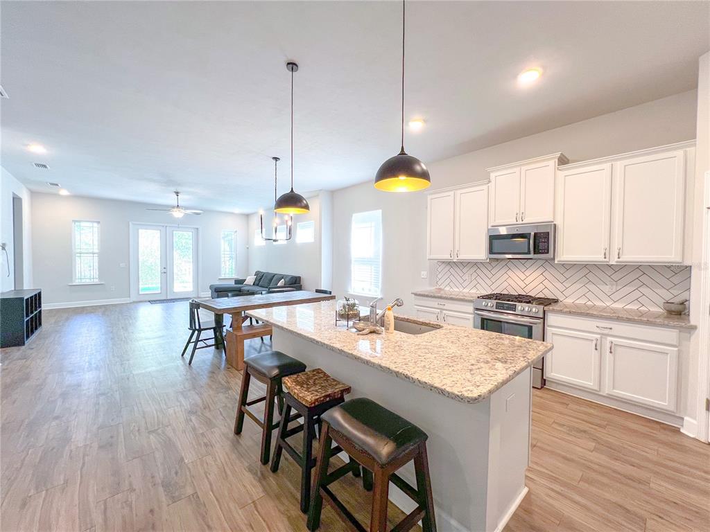 9340 Southwest 67th Lane Gainesville, FL 32608 - Photo 4 of 16 a kitchen with stainless steel appliances granite countertop a stove a refrigerator a kitchen island a sink and white cabinets with wooden floor