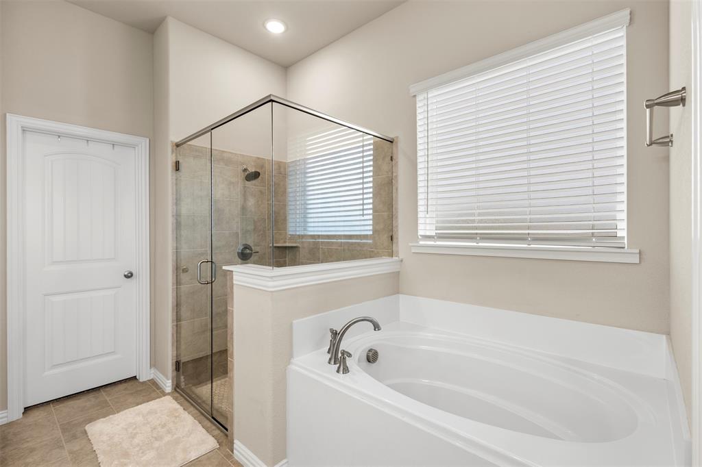 107 Yampa Court Rhome, TX 76078 - Photo 22 of 30 Bathroom featuring a built-in soaking tub with deck-mounted faucet, a walk-in shower with a glass enclosure and tiled walls, and a window with white blinds