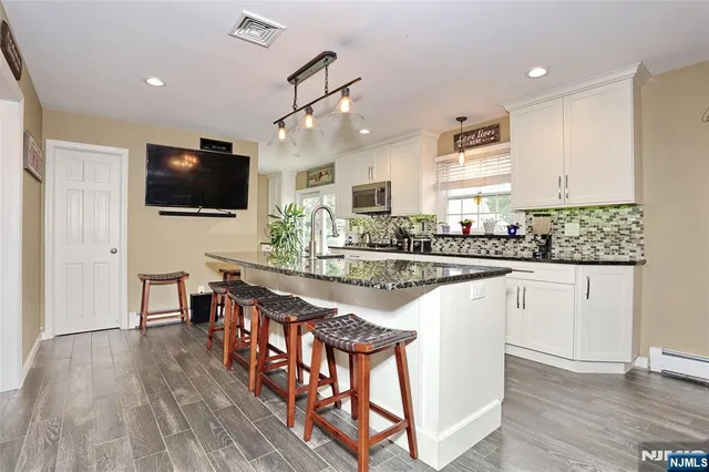 a kitchen with stainless steel appliances granite countertop a stove top oven a sink dishwasher a refrigerator and a dining table with wooden floor