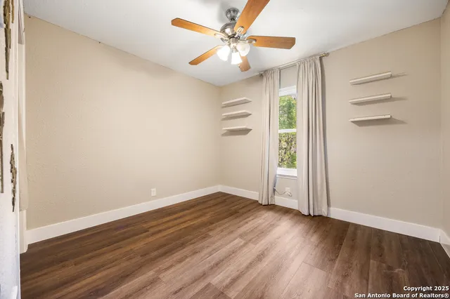 an empty room with wooden floor chandelier fan and windows