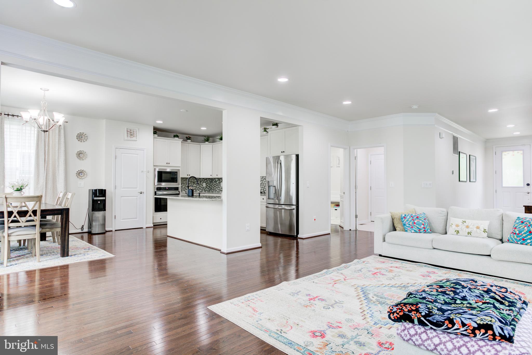 22800 Bubbling Brook Drive Brambleton, VA 20148 - Photo 21 of 64 a large white kitchen with stainless steel appliances kitchen island a stove a refrigerator a sink and a dining table with wooden floor