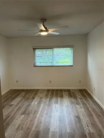 an empty room with wooden floor chandelier fan and windows