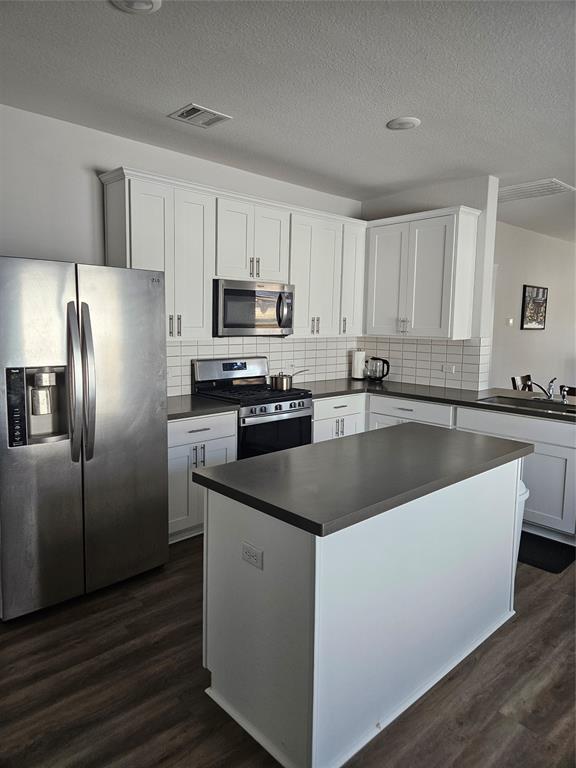 312 Gidran Trail Georgetown, TX 78626 - Photo 6 of 14 Kitchen featuring white cabinetry with brushed nickel hardware, a stainless steel appliance suite, dark countertops, white subway tile backsplash, and wood-finish flooring