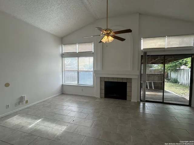 a view of a livingroom with a fireplace a ceiling fan and windows