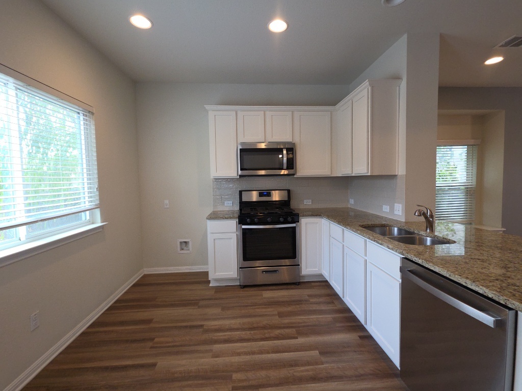 18009 Malnati Drive Pflugerville, TX 78660 - Photo 4 of 22 a kitchen with granite countertop a stove top oven a sink and dishwasher a refrigerator with wooden floors