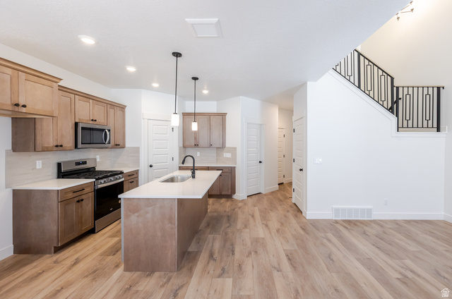 4809 Olive Avenue, Unit 417 Mapleton, UT 84664 - Photo 8 of 18 Kitchen with stainless steel appliances, a center island with sink, light stone counters, light wood-style flooring, and decorative light fixtures