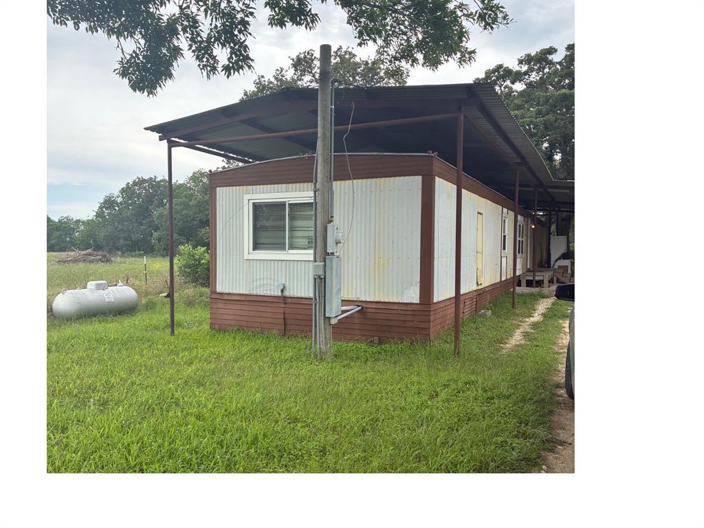 Exterior featuring white corrugated siding with brown trim, a metal awning extending the length of the structure, and a window with horizontal blinds