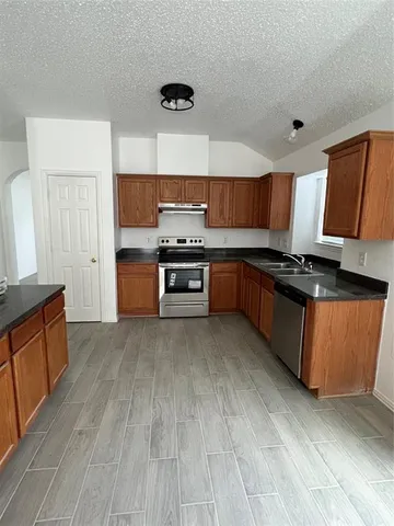 a kitchen with stainless steel appliances granite countertop a stove a sink dishwasher and a refrigerator with wooden floor