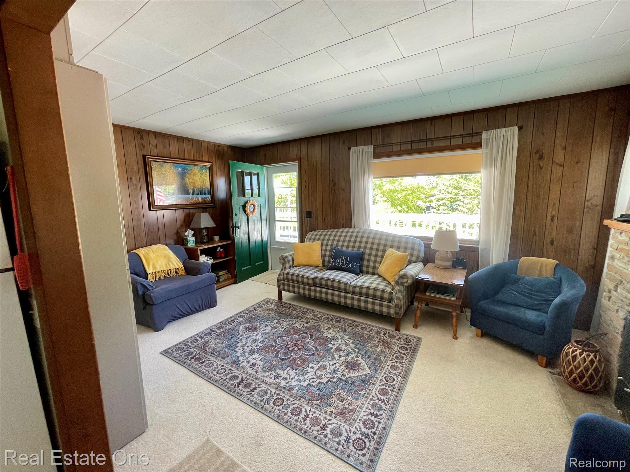 4160 Hawk Road Lincoln, MI 48742 - Photo 17 of 48 Carpeted living area featuring wood paneling, a fireplace with a brick surround, and a green entry door