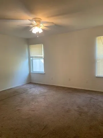 an empty room with a chandelier fan and windows