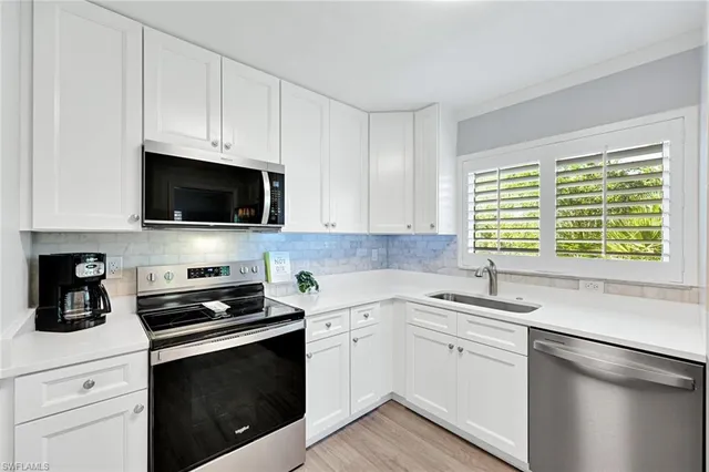 a kitchen with white cabinets appliances a sink and a window