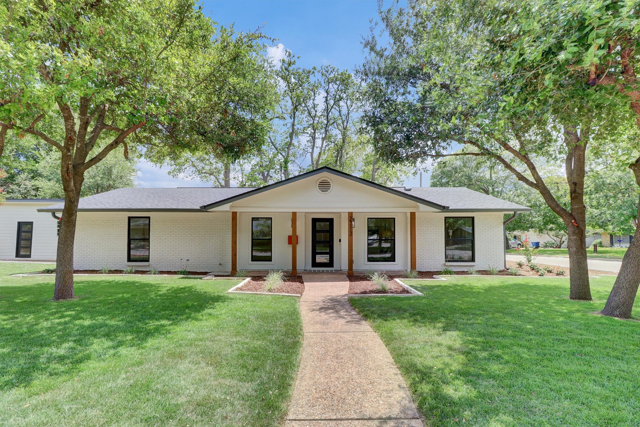 View of front of property featuring a front lawn, a porch, brick siding, and a shingled roof