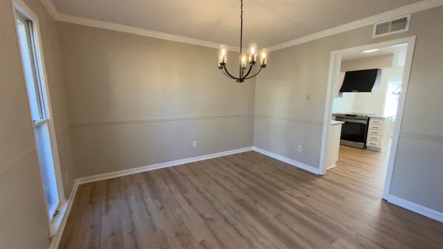 a view of empty room with wooden floor and kitchen