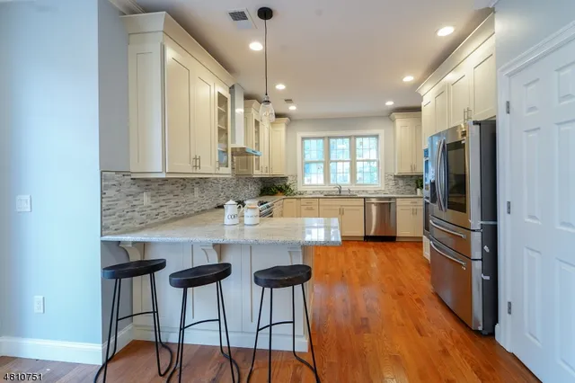 a kitchen with stainless steel appliances granite countertop a refrigerator a stove a sink dishwasher and white cabinets with wooden floor