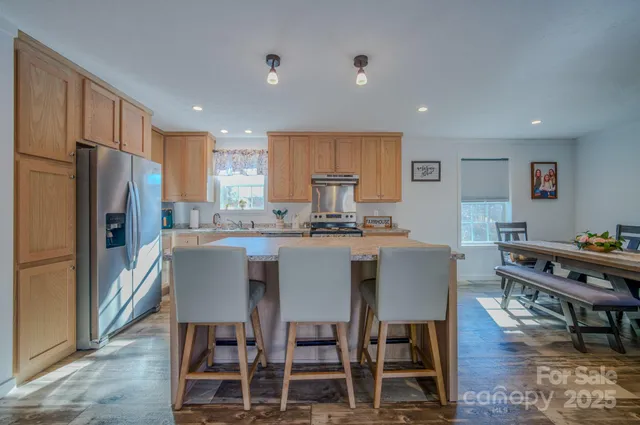 a kitchen with stainless steel appliances granite countertop a dining table chairs refrigerator and sink