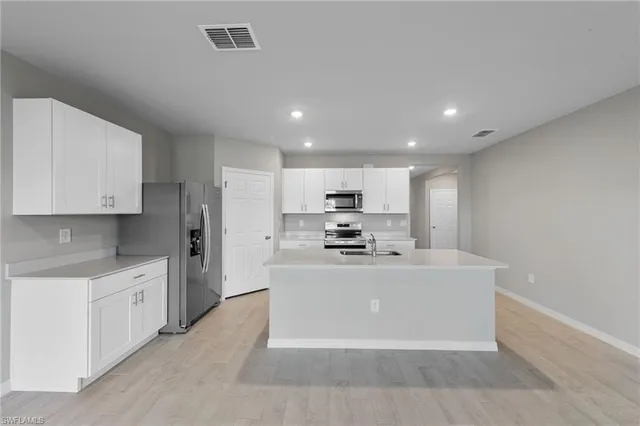 a large kitchen with stainless steel appliances a sink a stove a refrigerator and white cabinets