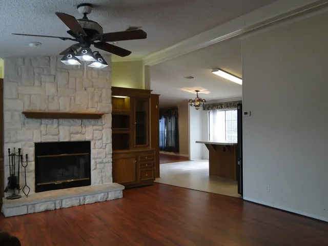 a view of a livingroom with a fireplace a ceiling fan and wooden floor