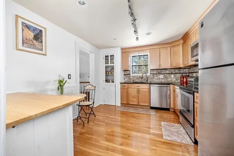 a kitchen with stainless steel appliances granite countertop a refrigerator a sink dishwasher a stove with white cabinets and wooden floor