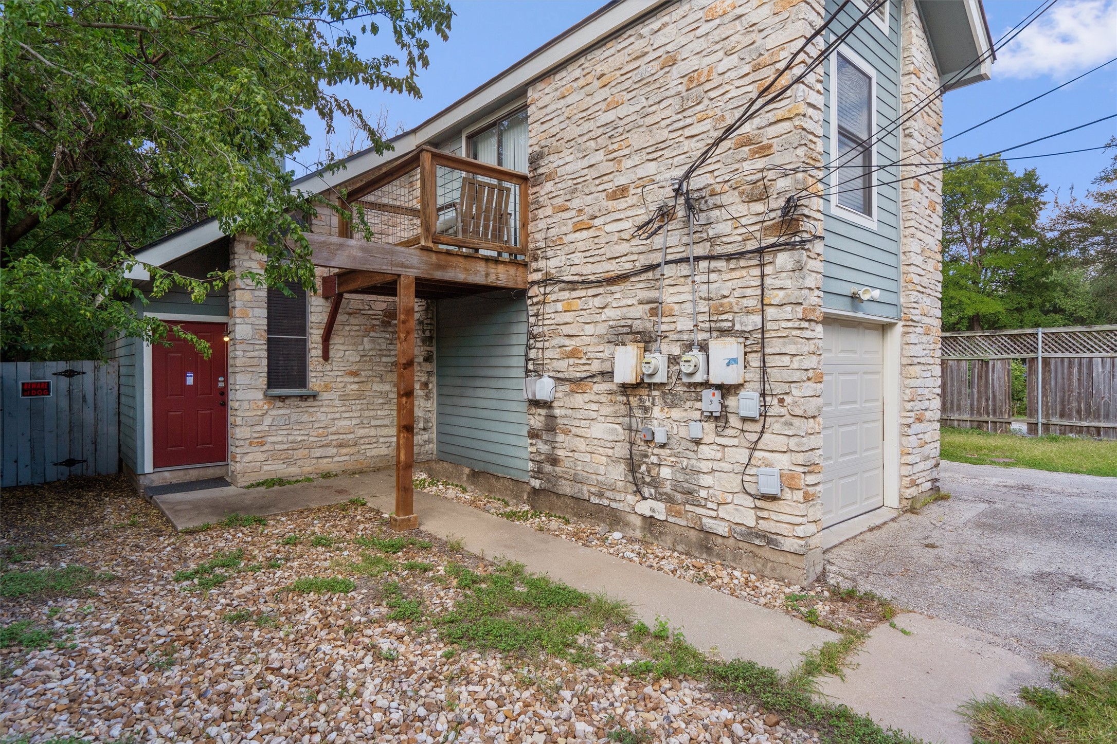 2414 Jones Road Austin, TX 78745 - Photo 2 of 26 A quaint stone and siding exterior features a red entry door, a second-story balcony, and a garage.