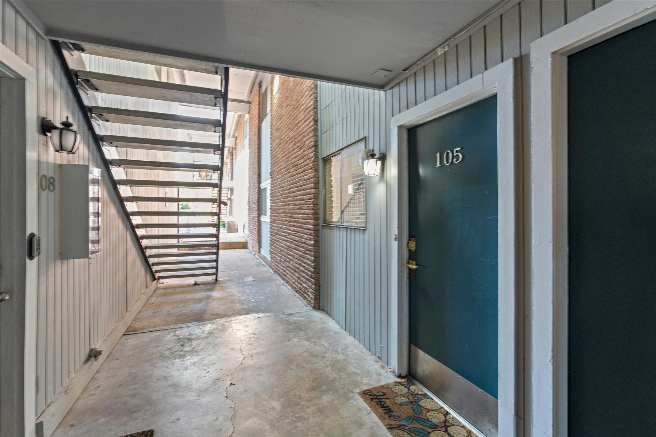 2208 Enfield Road, Unit 10500 Austin, TX 78703 - Photo 8 of 34 Covered exterior walkway featuring concrete flooring, vertical siding, a red brick accent wall, and an open metal staircase