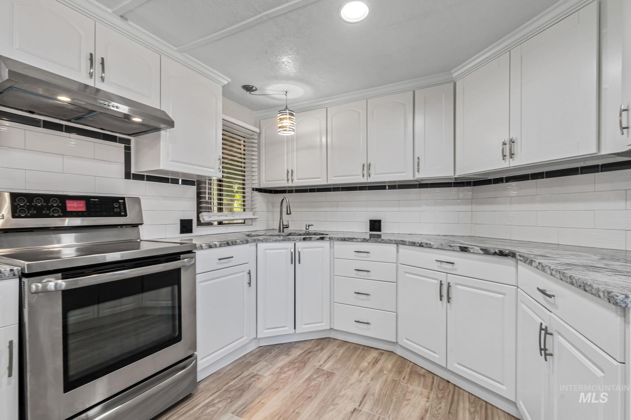 Kitchen with stainless steel electric stove, under cabinet range hood, white cabinets, decorative backsplash, and recessed lighting