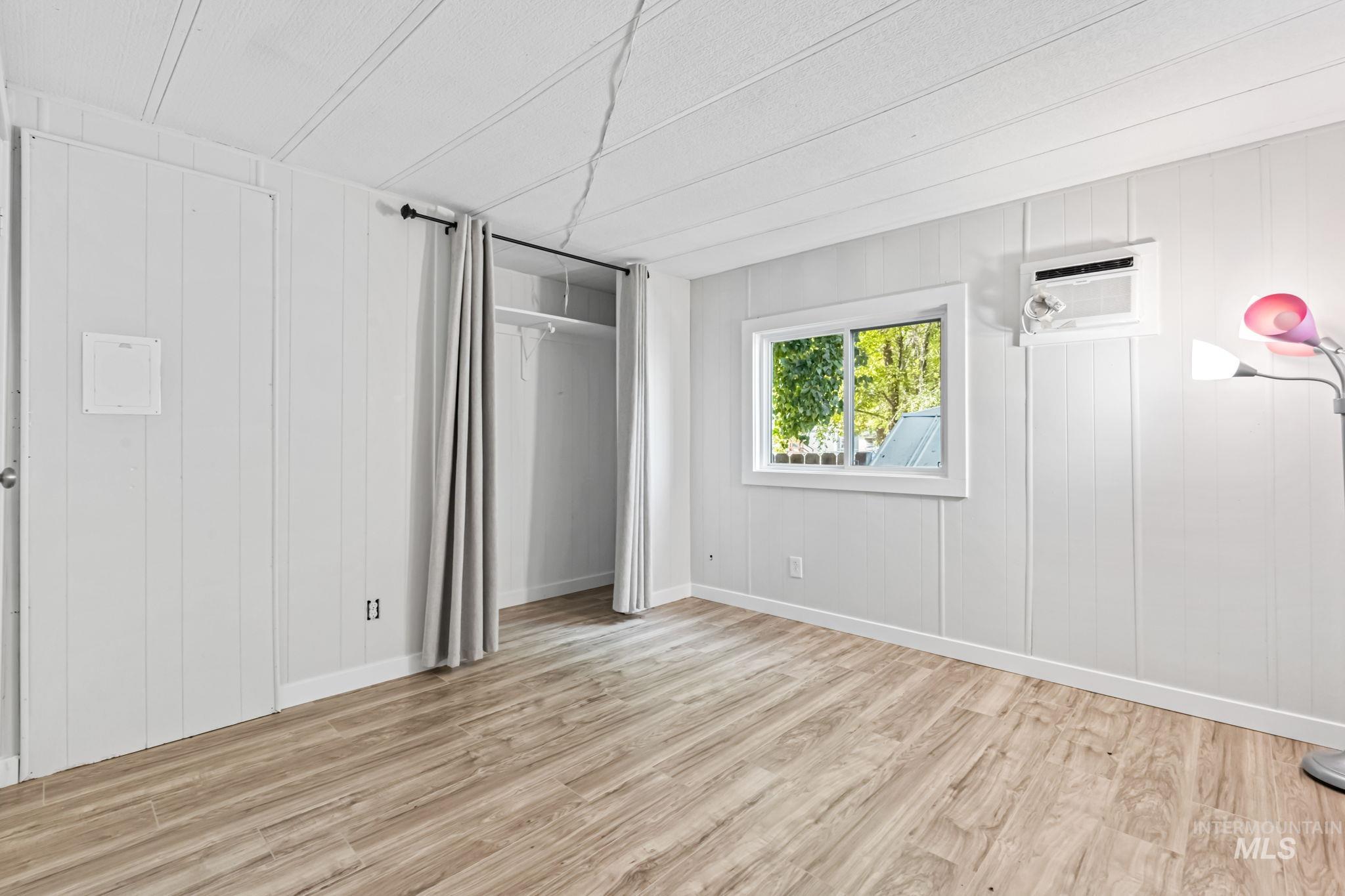 5015 East Ustick Road, Unit 181 Caldwell, ID 83605 - Photo 18 of 28 Unfurnished bedroom with light wood-style flooring, wooden walls, and a wall unit AC