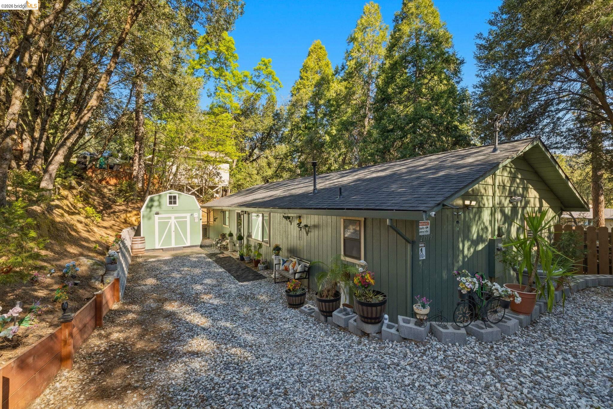 View of front facade with roof with shingles, a shed, view of scattered trees, and driveway