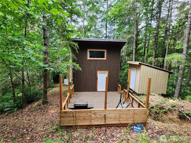 a view of a small house with a wooden deck and yard