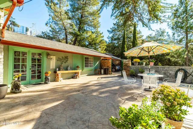 a view of a patio with table and chairs under an umbrella with large trees