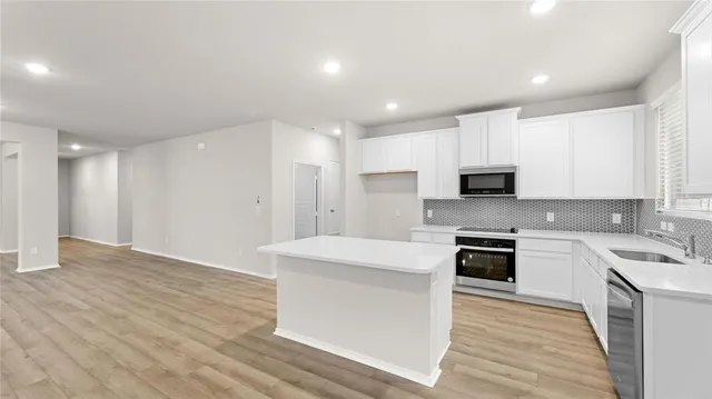 a kitchen with stainless steel appliances a stove top oven a sink dishwasher and a refrigerator with wooden floor