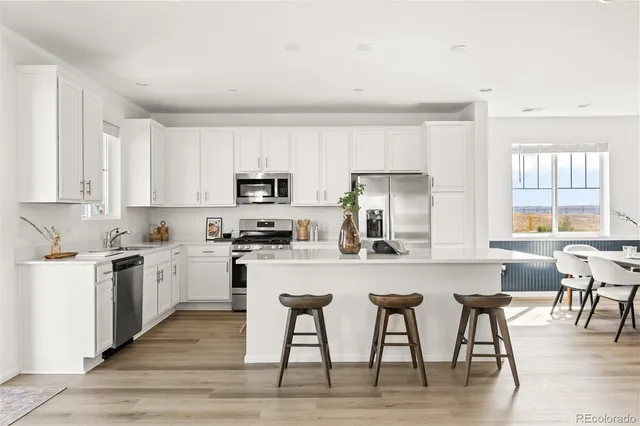 a kitchen with stainless steel appliances granite countertop a stove top oven a sink a refrigerator with white cabinets and wooden floor