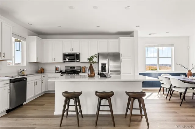 a kitchen with stainless steel appliances granite countertop a stove top oven a sink a refrigerator with white cabinets and wooden floor