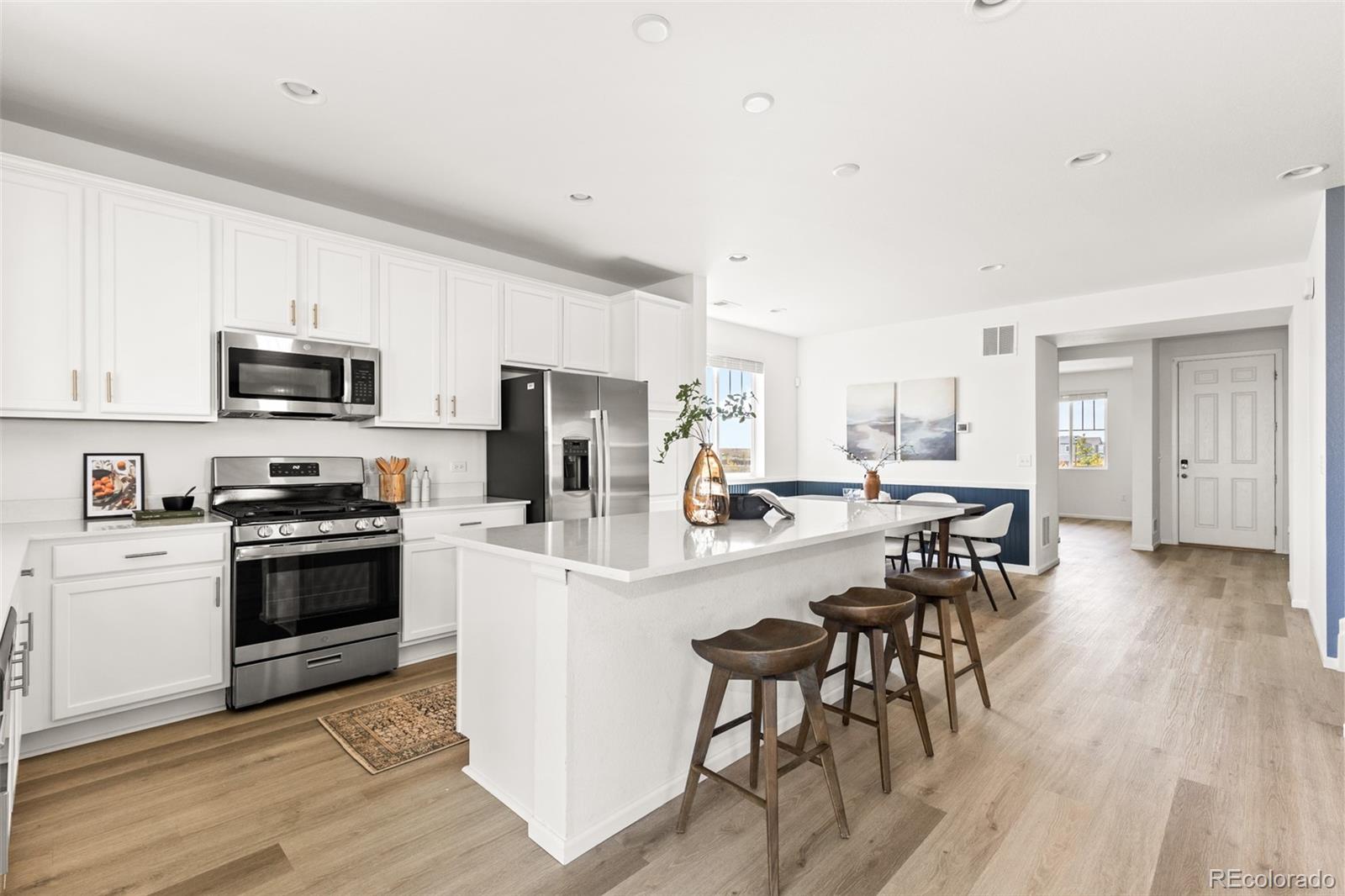 9054 Truckee Court Commerce City, CO 80022 - Photo 10 of 49 a kitchen with stainless steel appliances a microwave a stove a sink a refrigerator and white cabinets with wooden floor