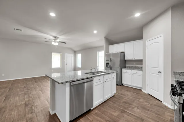 a kitchen with stainless steel appliances kitchen island granite countertop a stove a sink and white cabinets with wooden floor