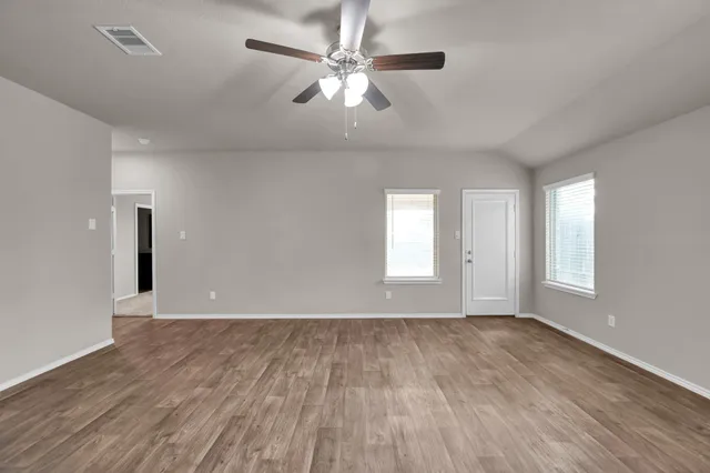 an empty room with wooden floor chandelier fan and windows