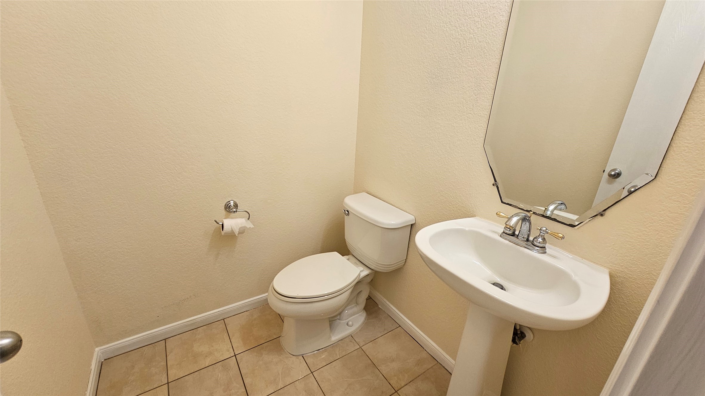 7918 Barnes Ridge Lane Houston, TX 77072 - Photo 27 of 34 This photo shows a compact bathroom with a pedestal sink, modern faucet, toilet, and a wall-mounted mirror. The floor is tiled, and the walls are painted in a light, neutral color.