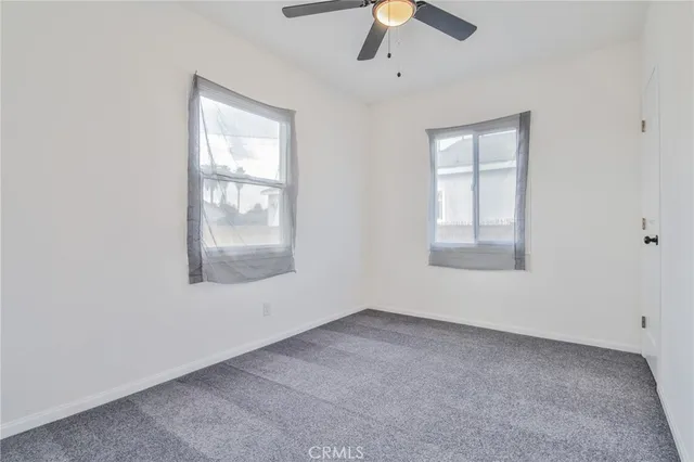 an empty room with chandelier fan and windows